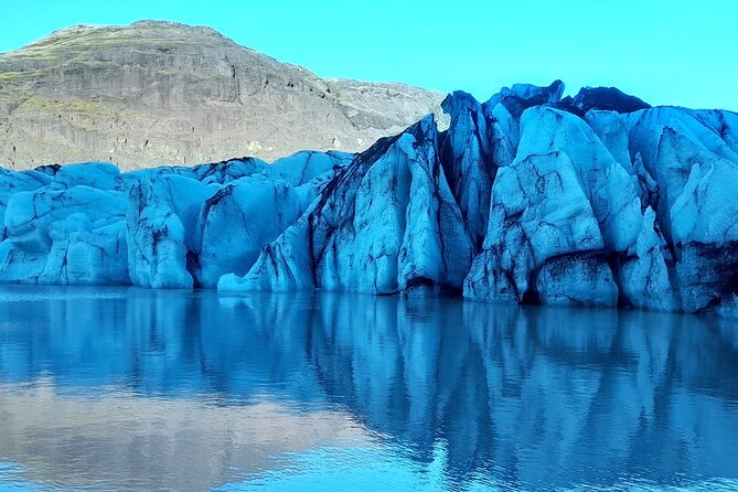 Blue glacier ice meeting the still water of a small meltwater lagoon