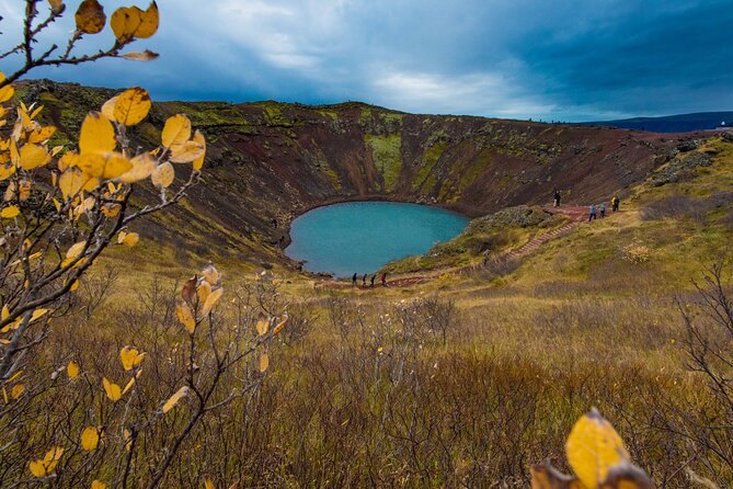 The aquamarine lake inside the Kerid crater, framed by red rock and autumn leaves