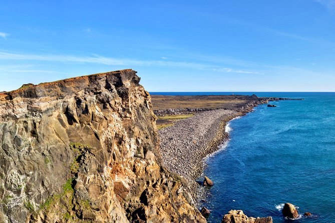 Sea cliffs on the Reykjanes peninsula dropping to a stony shore and clear green water