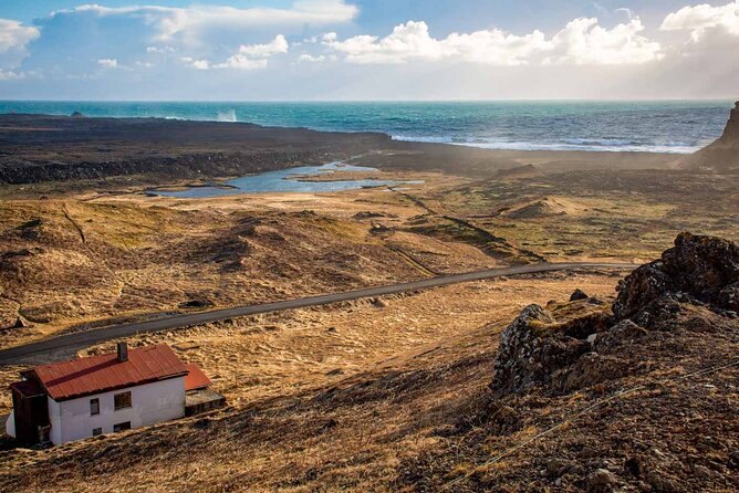 A red-roofed farm below moss-brown hills, with the road and the sea beyond